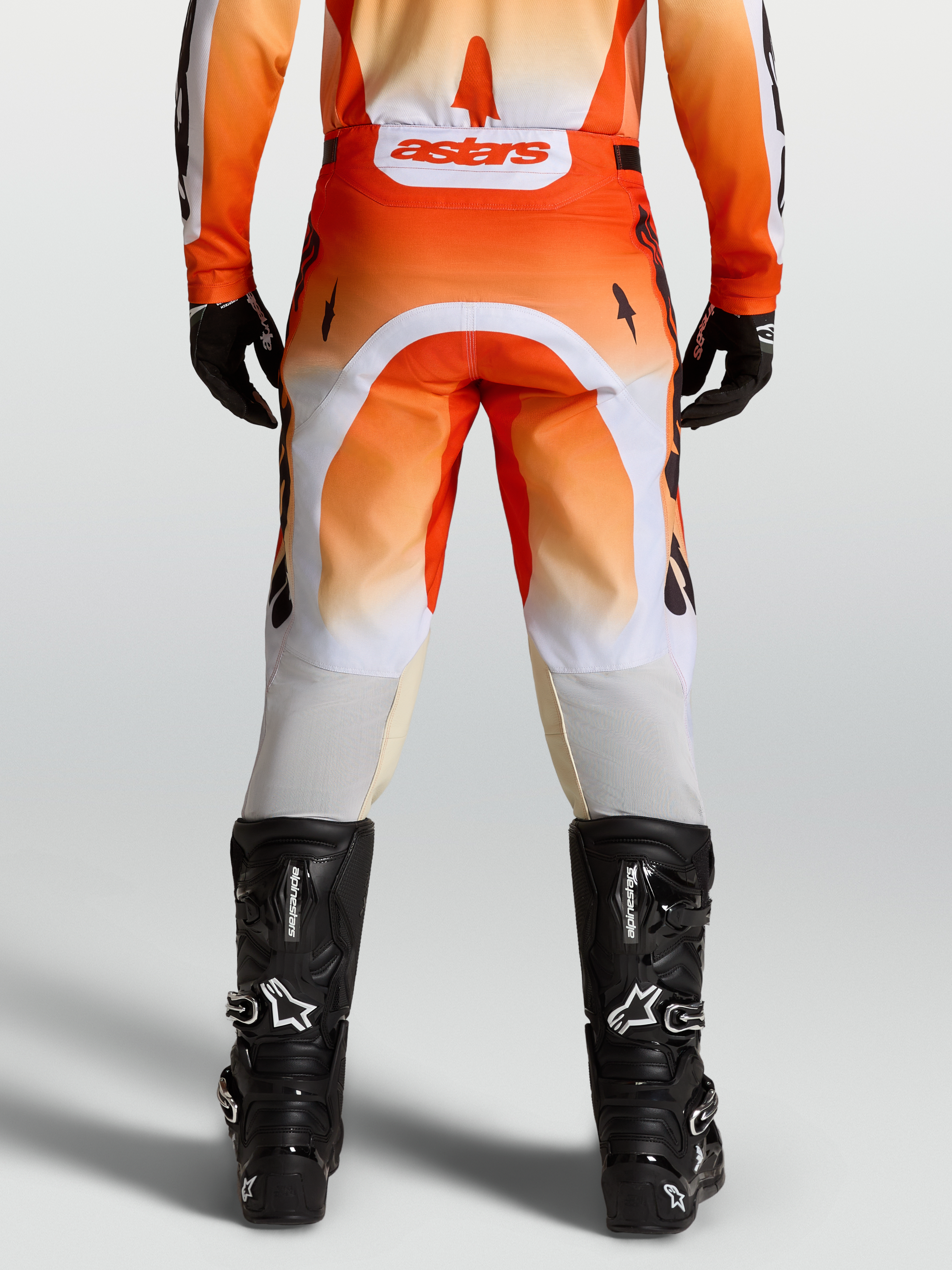 Alpinestars Racer Amber broek, motocrossbroek in rood en wit, achteraanzicht op model met zwarte motorlaarzen.