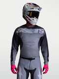 Alpinestars Racer Amber jersey, heren motorcross racingjersey, grijs en houtskool, vochtafvoerend polyfabric, gedragen met bijpassende broek, helm en felroze handschoenen.
