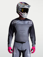 Alpinestars Racer Amber jersey, heren motorcross racingjersey, grijs en houtskool, vochtafvoerend polyfabric, gedragen met bijpassende broek, helm en felroze handschoenen.