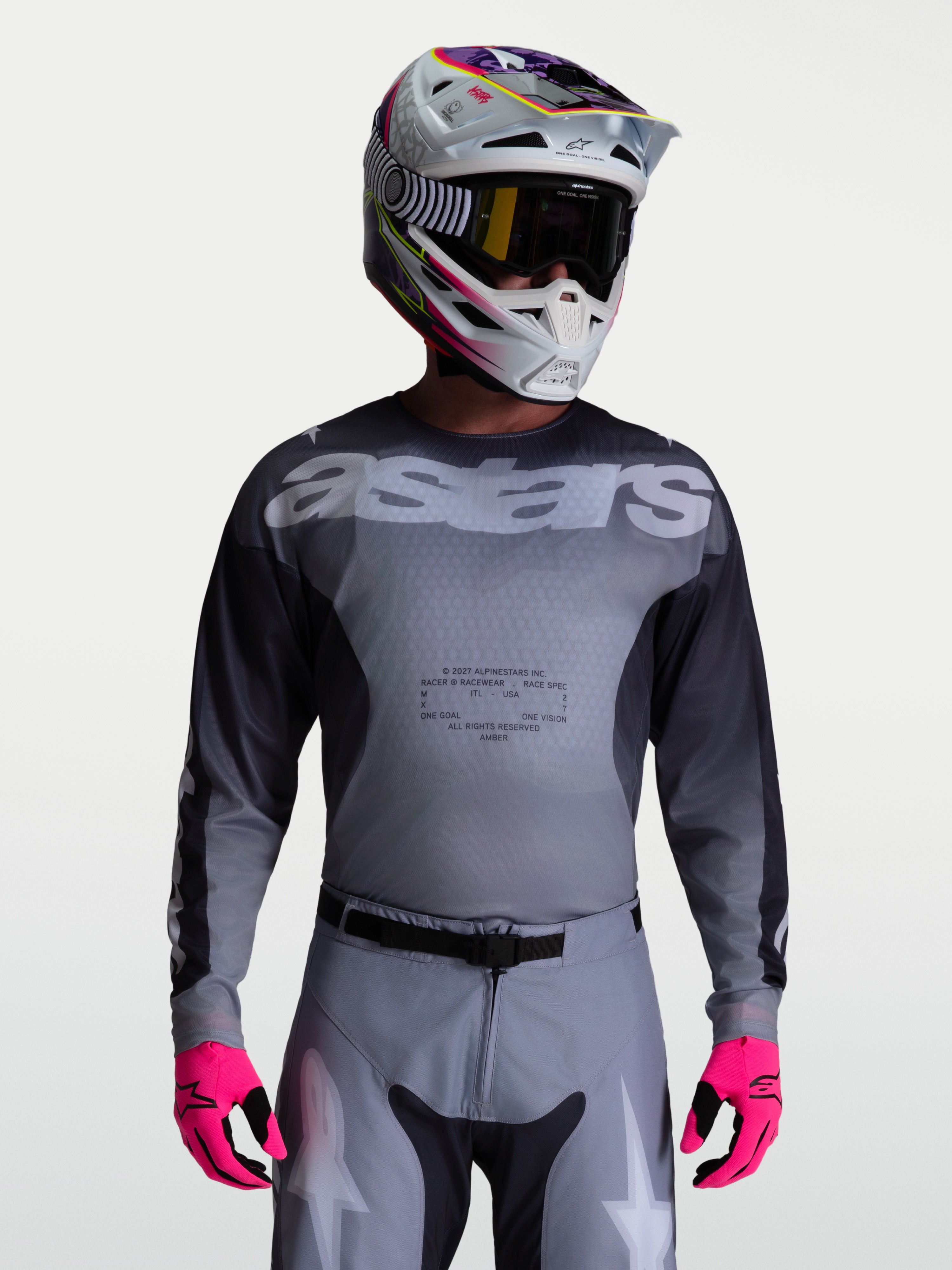 Alpinestars Racer Amber jersey, heren motorcross racingjersey, grijs en houtskool, vochtafvoerend polyfabric, gedragen met bijpassende broek, helm en felroze handschoenen.