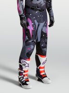 Alpinestars Racer Lone Broek, heren motorcrossbroek in grijs camo en paars, gedragen door model met laarzen, 600D polyweefsel en ergonomische stretch voor off-road prestaties.
