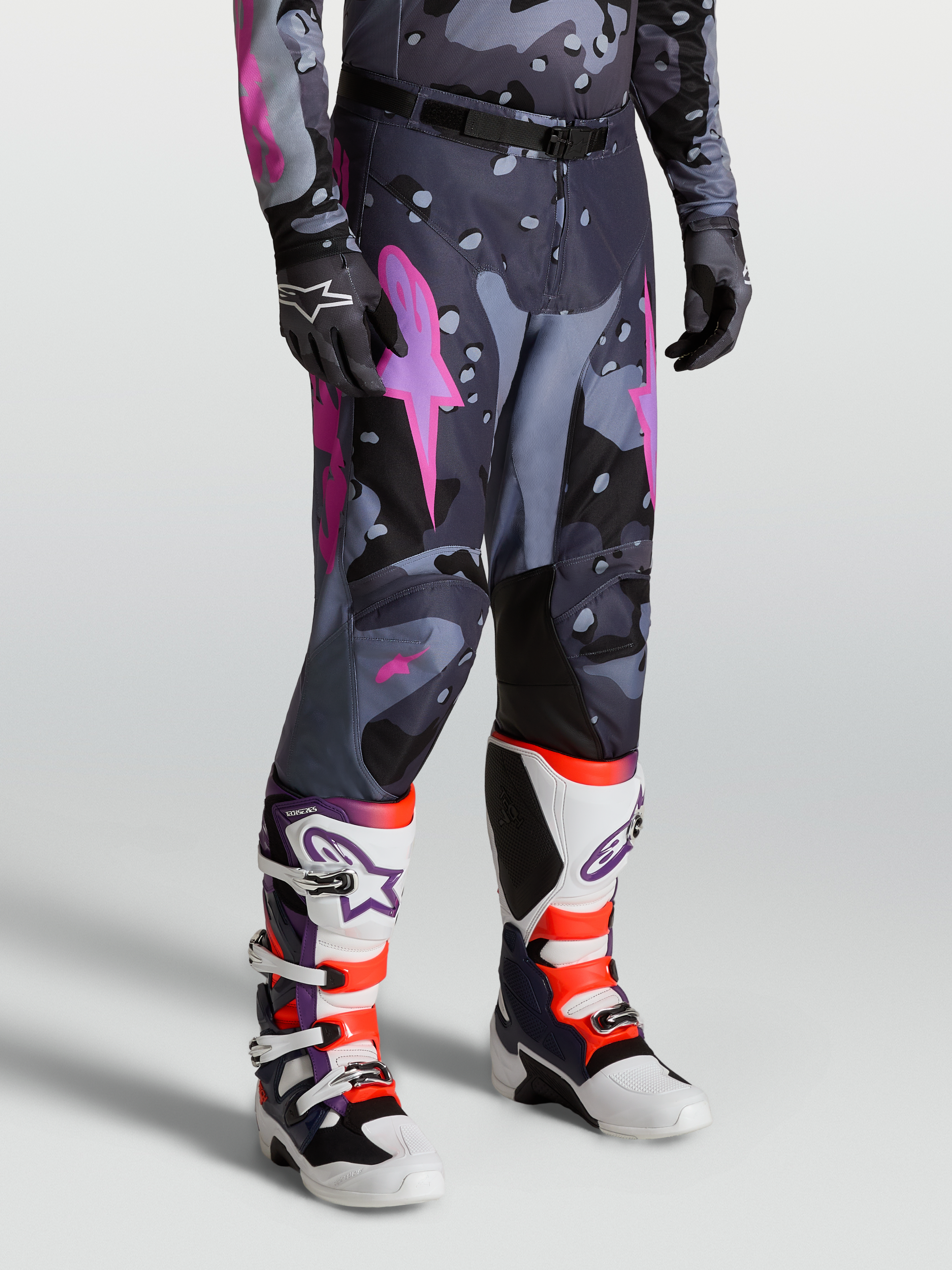 Alpinestars Racer Lone Broek, heren motorcrossbroek in grijs camo en paars, gedragen door model met laarzen, 600D polyweefsel en ergonomische stretch voor off-road prestaties.