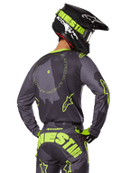 Motocross rider seen from behind wearing the 2025 Racer Hollow Gear Set, Gray jersey with fluorescent yellow circular text and star logos, matching gray and yellow pants with bold branding across the seat, black and lime green helmet, coordinated outfit for off-road racing