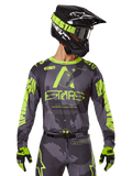 Alpinestars 2025 Racer Hollow Jersey, motorcross raceshirt, donkere camouflage en neongeel, gedragen met bijpassende broek, zwarte en gele helm met crossbril en zwarte handschoenen, voorzien van Alpinestars-branding en camouflage-ontwerp