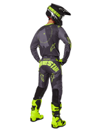 Motocrosser van achteren die de Alpinestars 2025 Racer Hollow Jersey en broek in Dark Camo Yellow Fluo draagt, voorzien van een donkergrijs camouflagepatroon met neongele accenten, gecombineerd met een bijpassende zwart-gele helm en fel neongele laarzen.