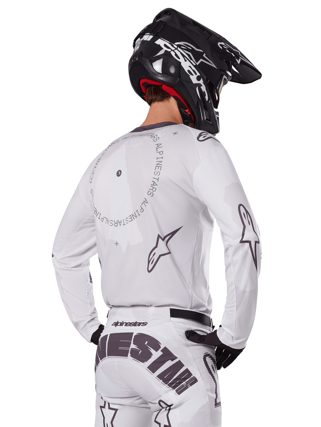 Motocrossrijder vanaf de achterkant in de Alpinestars 2025 Racer Hollow Gear Set in het wit, witte jersey met lange mouwen met grijze sterlogo's en cirkelvormige graphics, bijpassende witte broek met opvallende merknaam op het zitvlak, zwarte helm, gecoördineerde off-road race-uitrusting.