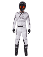 Alpinestars 2025 Racer Hollow Gear Set, wit met zwarte en grijze graphics, volledige motorcross race-outfit inclusief jersey en broek, gedragen met zwarte helm, oranje goggles, zwarte handschoenen en zwarte laarzen, hoogwaardige off-road kleding