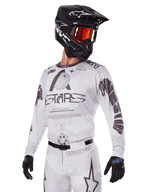 Alpinestars 2025 Racer Hollow Gear Set, motorcross jersey en broek, wit met zwarte en grijze graphics, voorzien van 'ASTARS' branding en hollow globe ontwerpen, gedragen met een zwarte helm, rode spiegelbril en zwarte handschoenen, ontworpen voor off-road prestaties