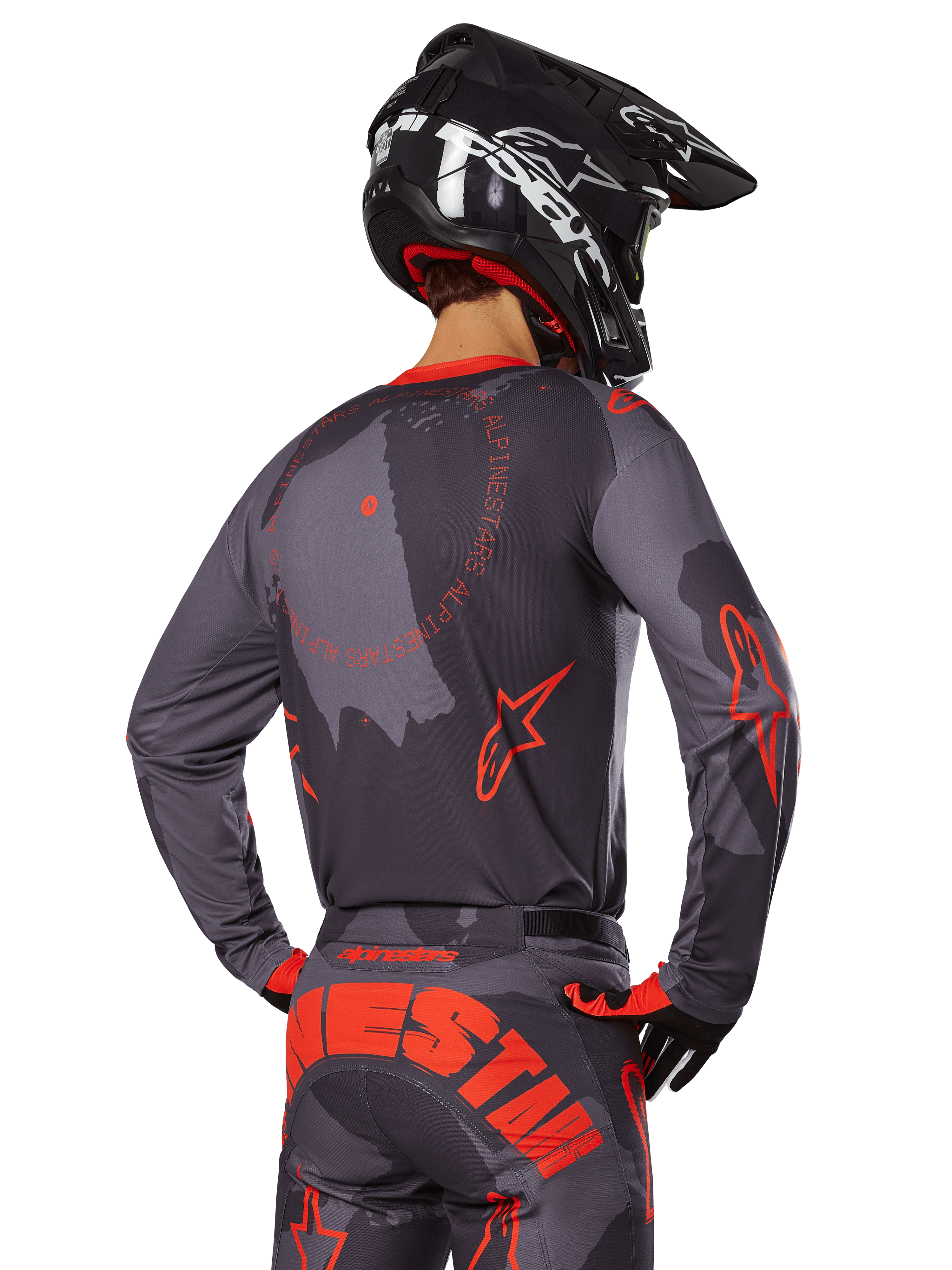Motocrossrijder van achteren gezien in volledige race-uitrusting, Gray Camo jersey met Orange Fluo accenten en ronde branding op de rug, bijpassende camouflagebroek met grote oranje Alpinestars-tekst op het zitvlak, zwarte helm en oranje met zwarte handschoenen, gecoördineerde outfit voor off-road racen