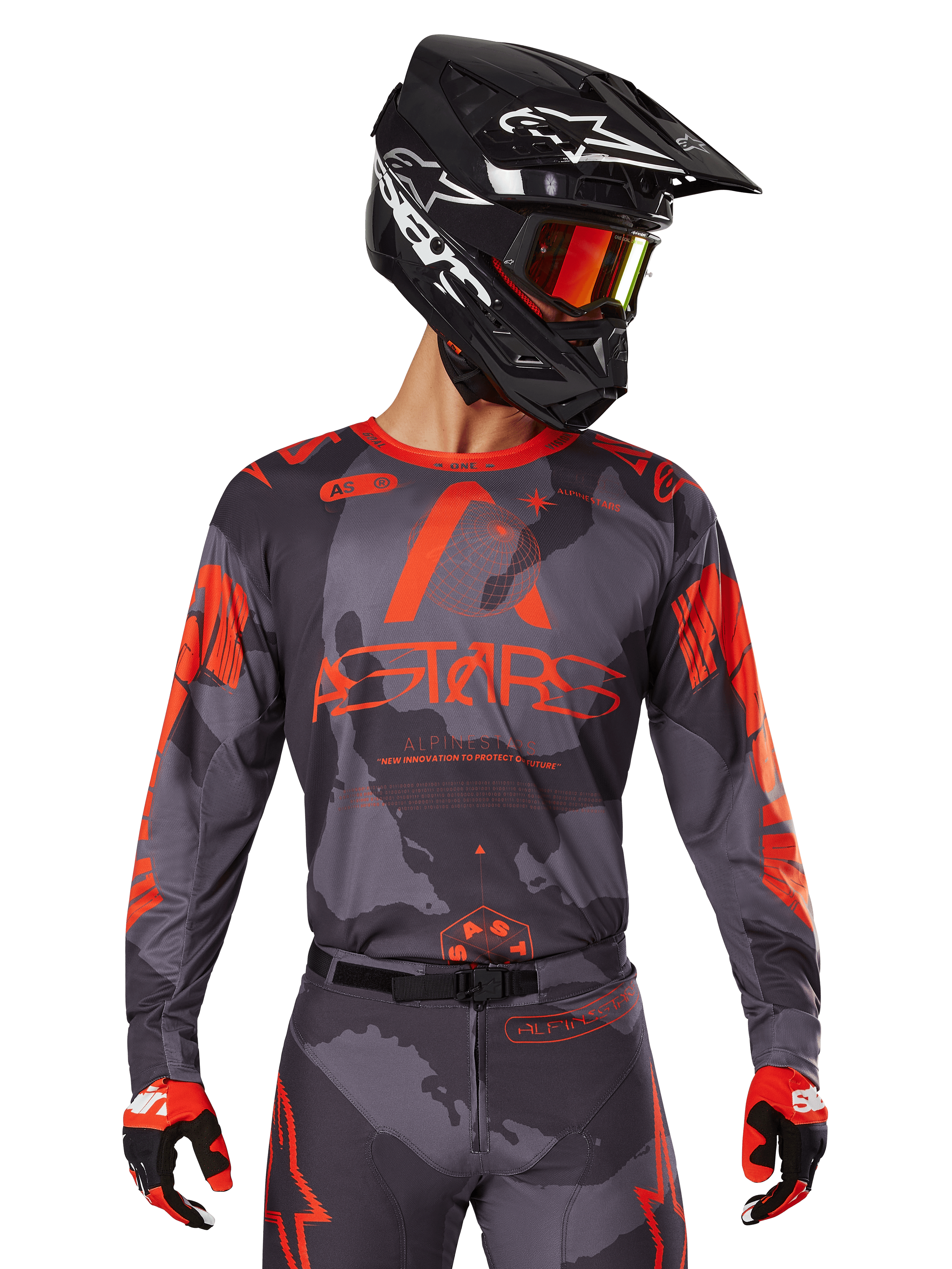 Alpinestars 2025 Racer Hollow Jersey, motorcross jersey, grijs camo en fluo oranje, gedragen met bijpassende kledingset inclusief broek en handschoenen, met een zwarte helm met witte graphics en crossbril, opvallende ASTARS-branding, beschermende off-road race-sportkleding