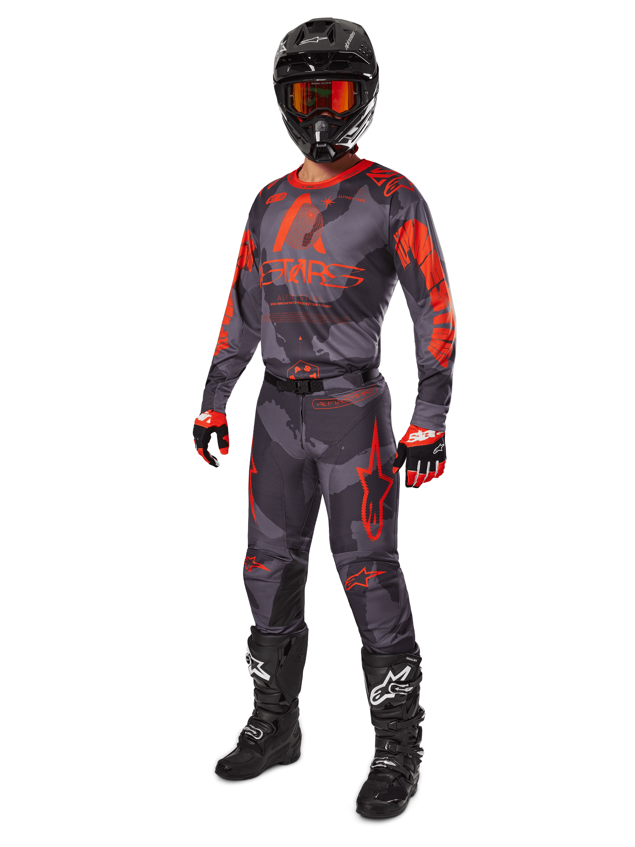 Motorcrossrijder in volledige race-uitrusting, Alpinestars 2025 Racer Hollow Jersey en broek in grijs camo en fluo oranje, zwarte helm met oranje bril, zwart-rode handschoenen en zwarte laarzen met witte logo's, gecoördineerde prestatie-outfit voor off-road racing