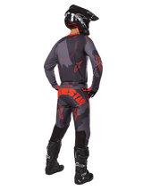 Motorcrosser van achteren gezien in de Alpinestars 2025 Racer Hollow Jersey in Gray Camo Orange Fluo, bijpassende camouflagebroek met oranje Alpinestars-tekst, zwarte helm en zwarte laarzen, gecoördineerde uitrustingsset voor off-road rijden