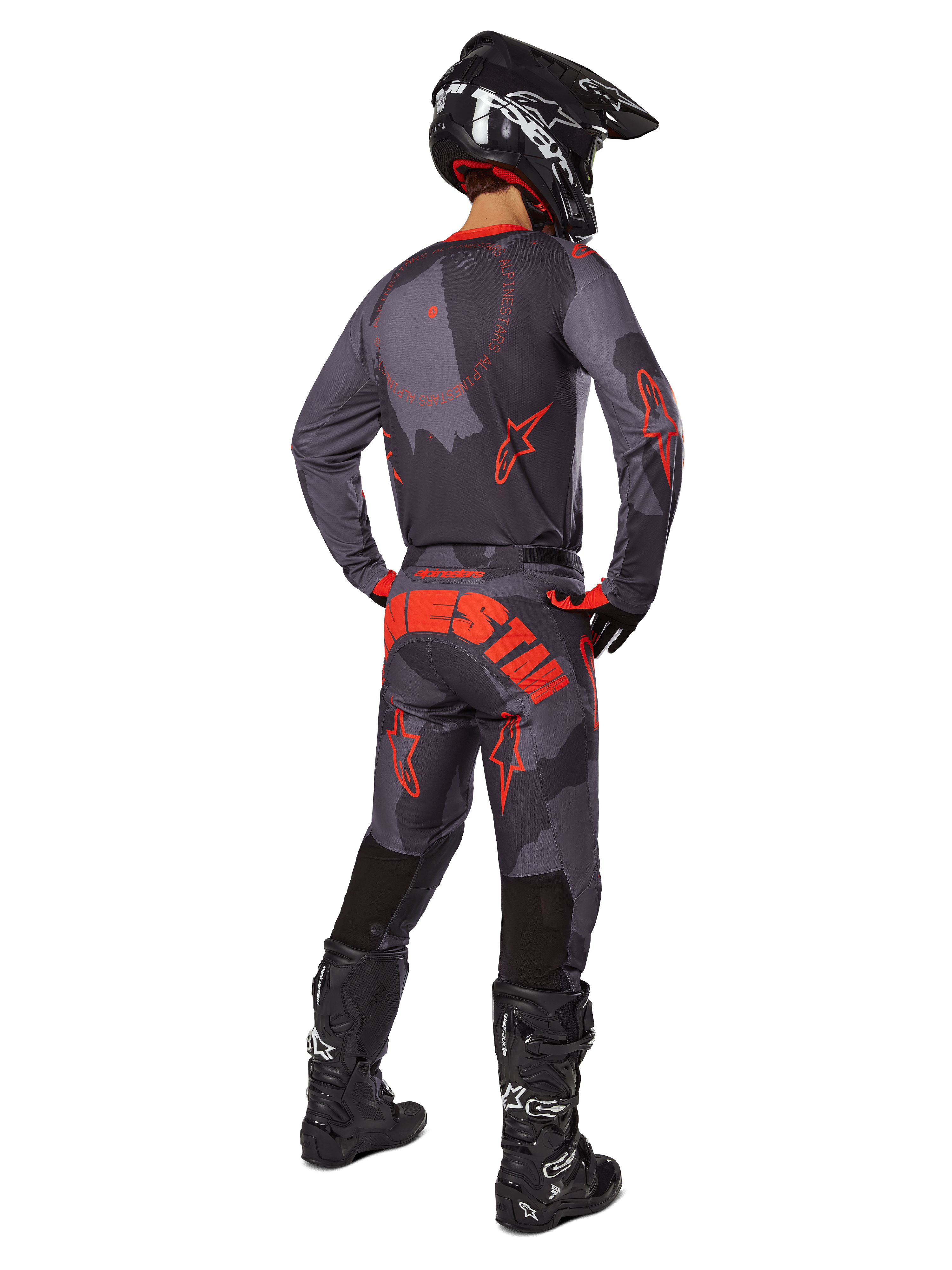 Motorcrosser van achteren gezien in de Alpinestars 2025 Racer Hollow Jersey in Gray Camo Orange Fluo, bijpassende camouflagebroek met oranje Alpinestars-tekst, zwarte helm en zwarte laarzen, gecoördineerde uitrustingsset voor off-road rijden