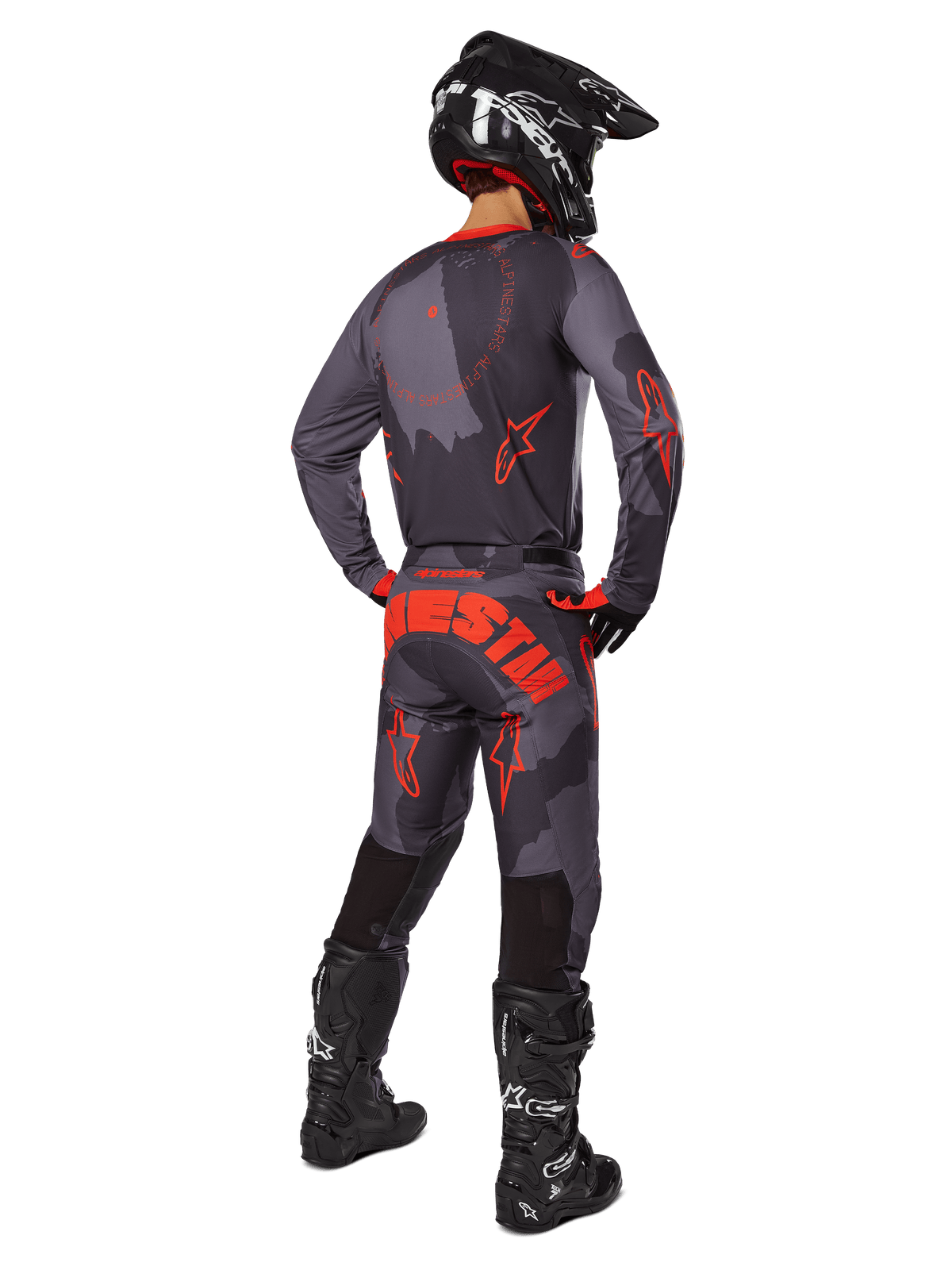 Motorcrosser van achteren die de Alpinestars 2025 Racer Hollow Gear Set draagt in Gray Camo Orange Fluo, met een grijs camouflagepatroon met feloranje branding, een zwarte helm en zwarte Tech-laarzen.