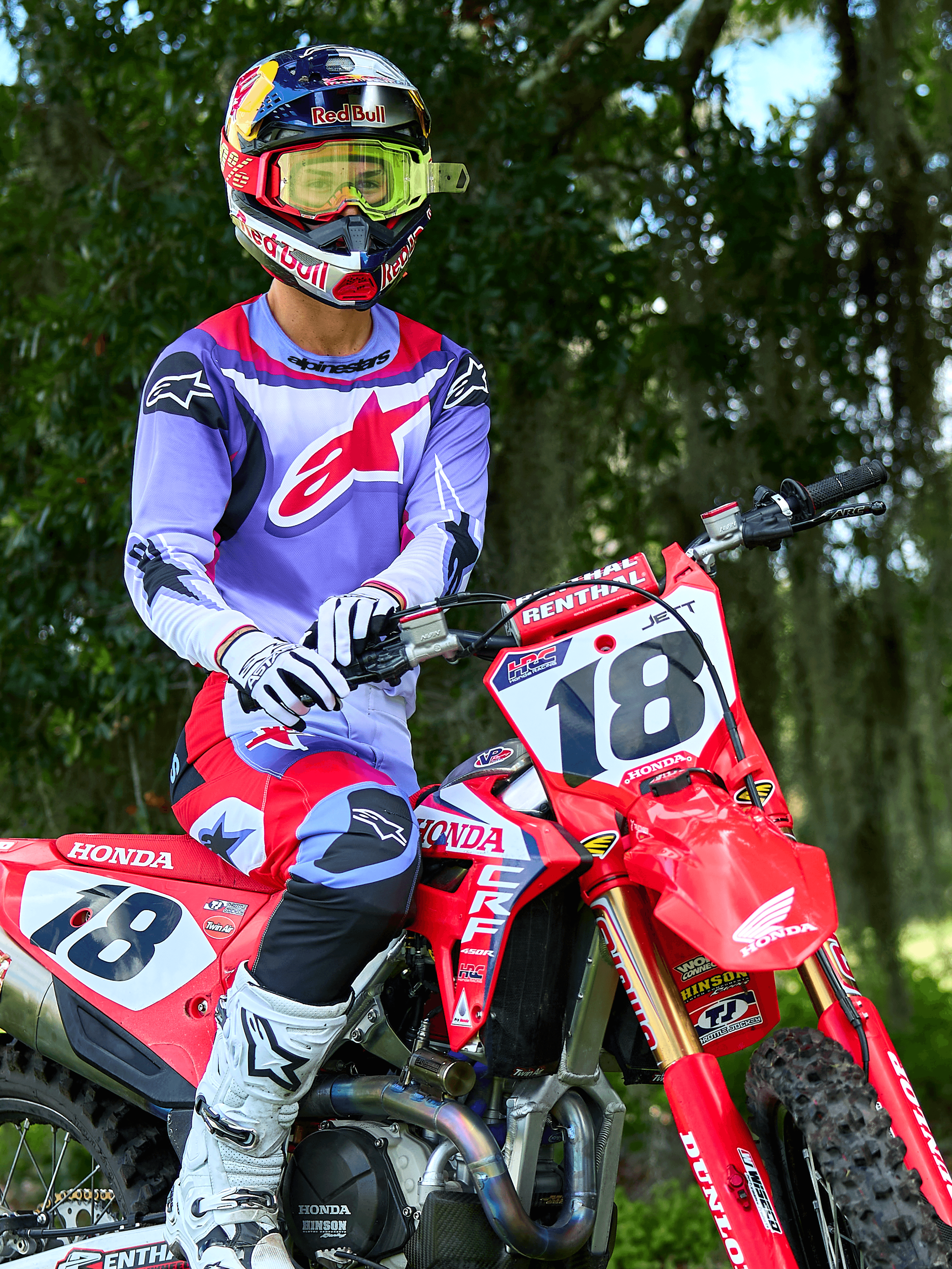 Motorcrosser op een rode Honda CRF crossmotor, draagt Alpinestars 2025 Fluid Wurx Jersey in paars en felrood, bijpassende paarse en rode broek, Red Bull-helm met gele crossbril, witte Alpinestars laarzen en handschoenen, professionele MX-uitrusting voor off-road rijden