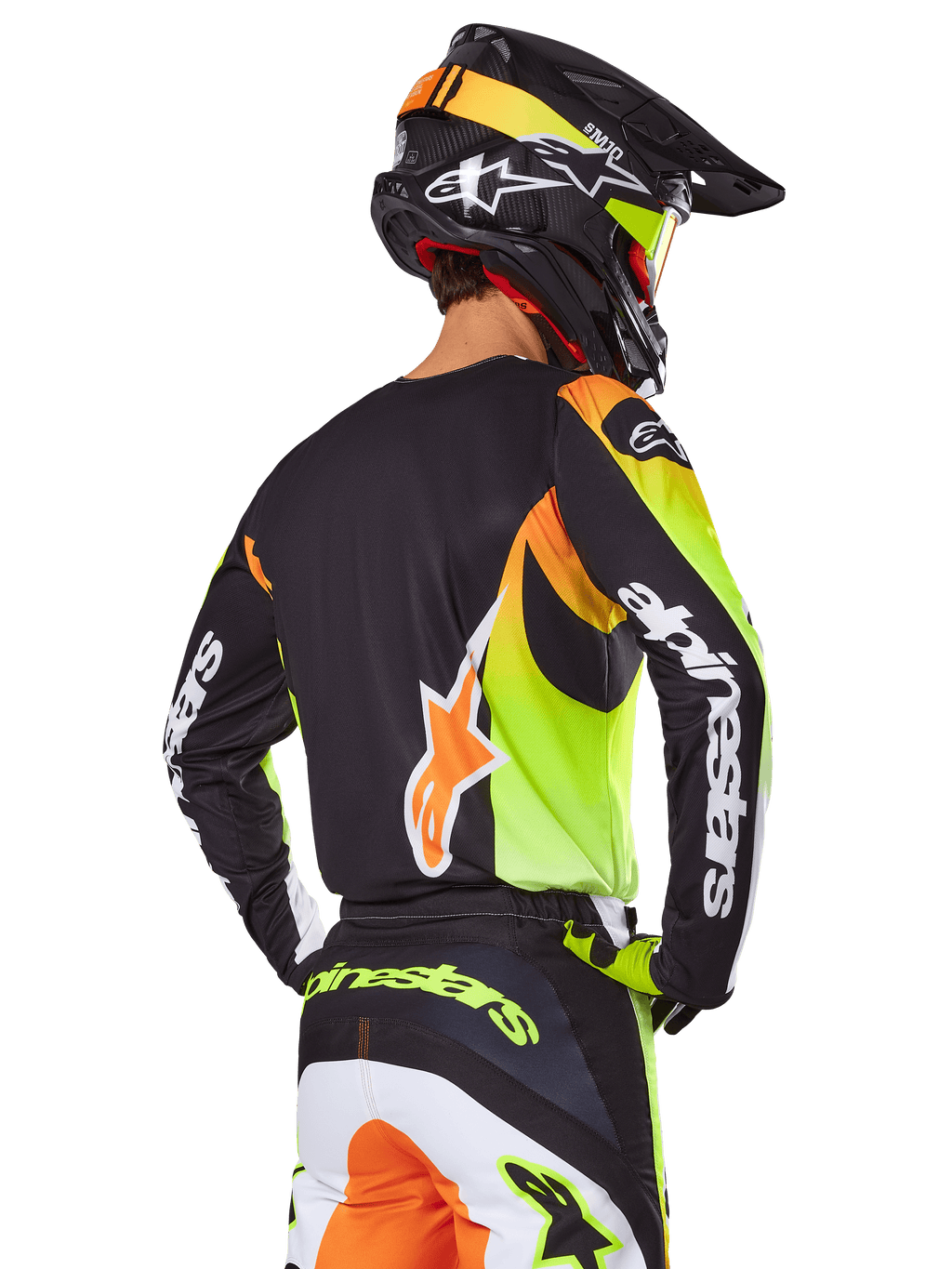 Alpinestars 2025 Fluid Wurx Gear Set, motorcrossrijder van achteren gezien, zwarte jersey met felle neongele en oranje graphics, bijpassende broek met witte en oranje panelen, zwarte helm met neonaccenten, opvallende Alpinestars branding op de mouwen en het zitvlak