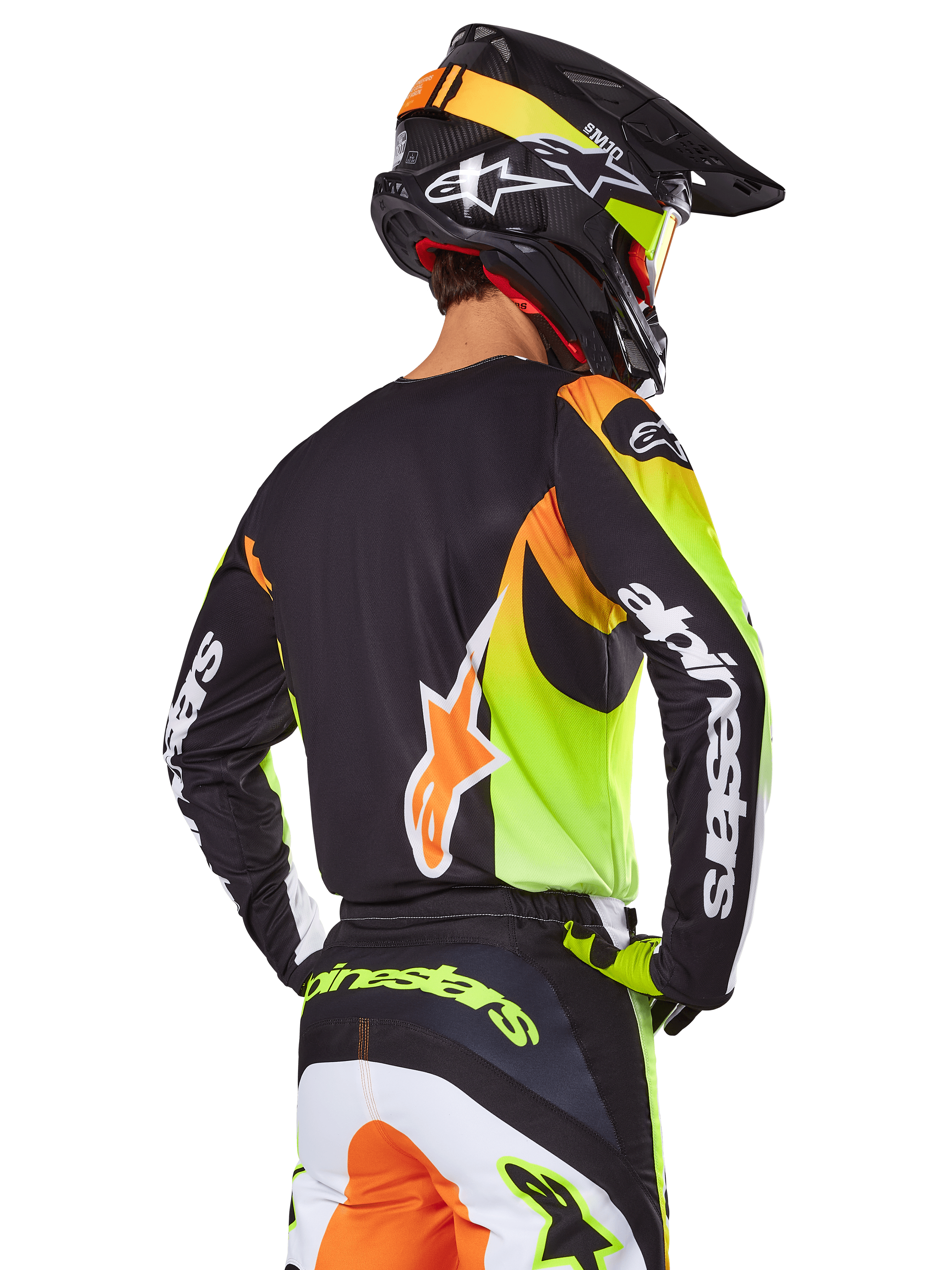 Alpinestars 2025 Fluid Wurx Gear Set, motorcrossrijder van achteren gezien, zwarte jersey met felle neongele en oranje graphics, bijpassende broek met witte en oranje panelen, zwarte helm met neonaccenten, opvallende Alpinestars branding op de mouwen en het zitvlak