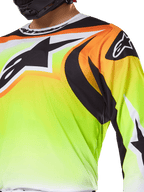 Alpinestars 2025 Fluid Wurx Jersey, motocross shirt, fluorescerend geel met zwarte en oranje graphics, groot zwart Alpinestars-logo op de borst en schouder, gedragen door een rijder met een zwarte helm