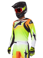Motocross-rijder in Alpinestars 2025 Fluid Wurx Gear Set, jersey met geel en oranje kleurverloop, zwarte accenten en grote sterlogo's, bijpassende motorcrossbroek, zwarte full-face helm met rood getinte bril en gele handschoenen, gecoördineerde high-performance outfit voor off-road racen