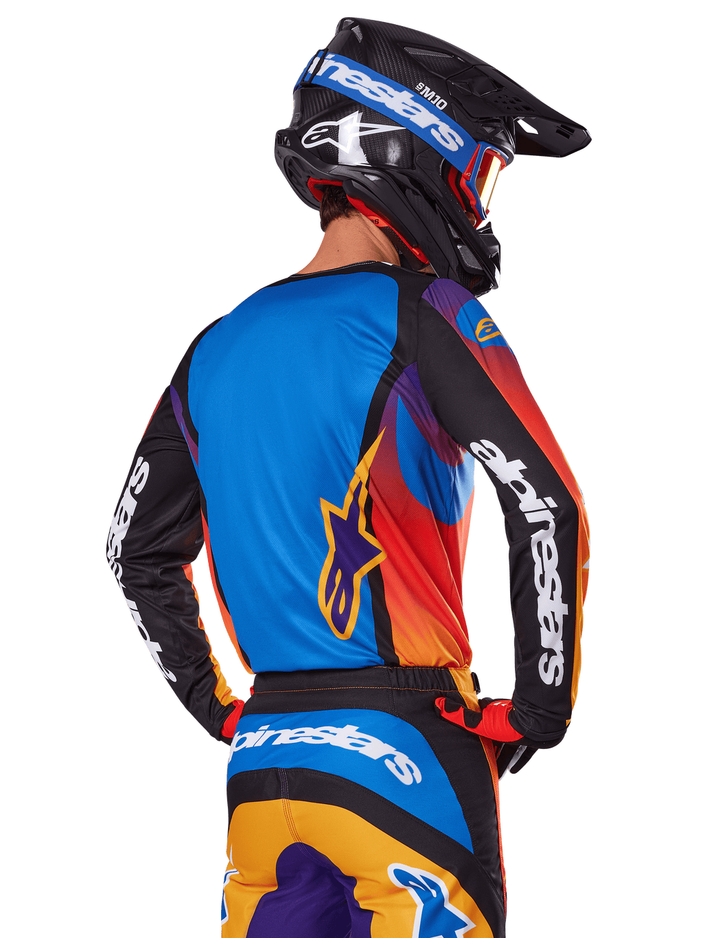 Alpinestars 2025 Fluid Wurx Gear Set, motorcrossrijder van achteren gezien, meerkleurige jersey met blauwe achterkant en zwarte mouwen met witte logo's, bijpassende oranje en blauwe broek, zwart-blauwe helm met oranje bril, gecoördineerde off-road race-outfit