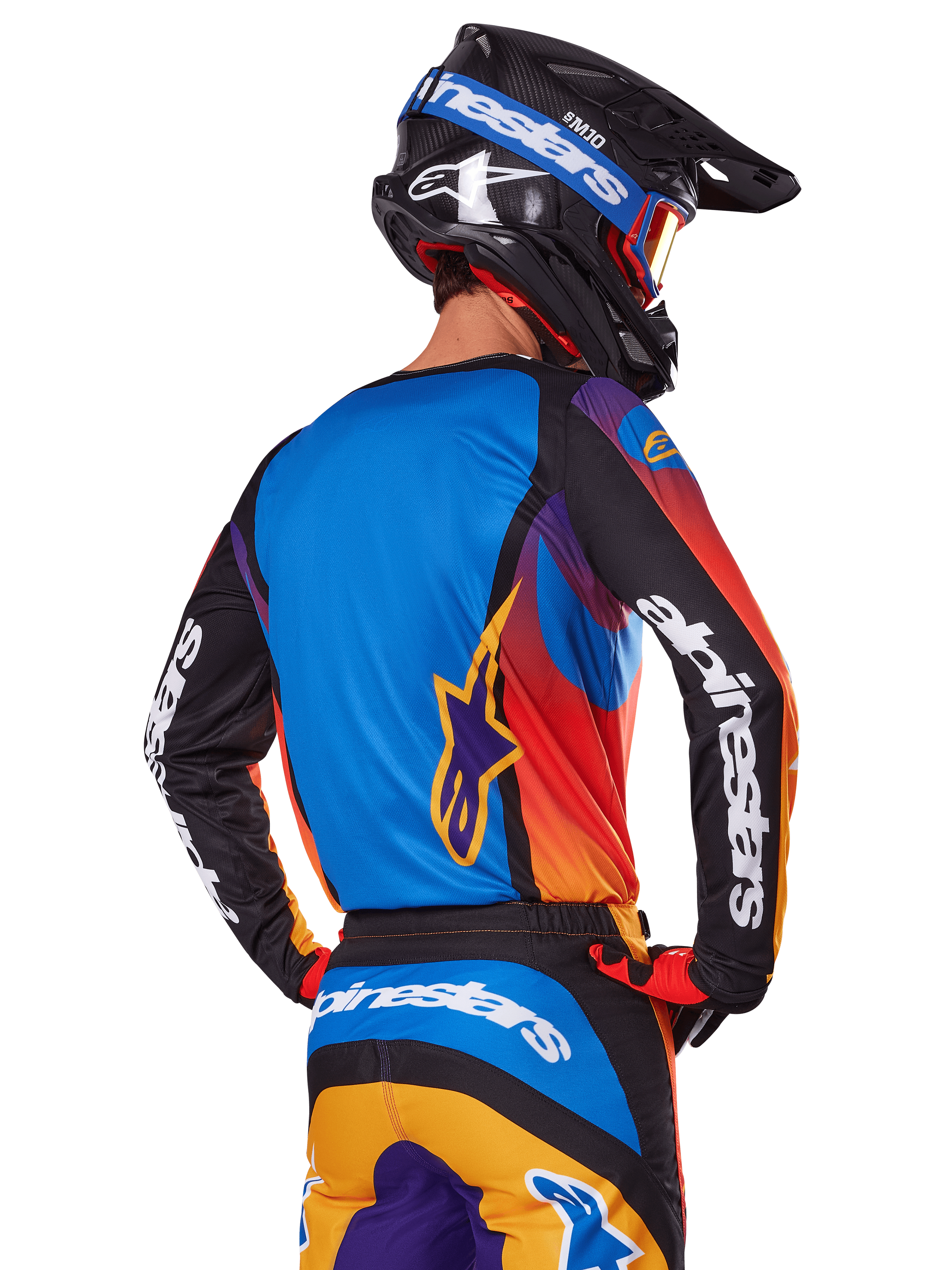 Alpinestars 2025 Fluid Wurx Gear Set, motorcrossrijder van achteren gezien, meerkleurige jersey met blauwe achterkant en zwarte mouwen met witte logo's, bijpassende oranje en blauwe broek, zwart-blauwe helm met oranje bril, gecoördineerde off-road race-outfit
