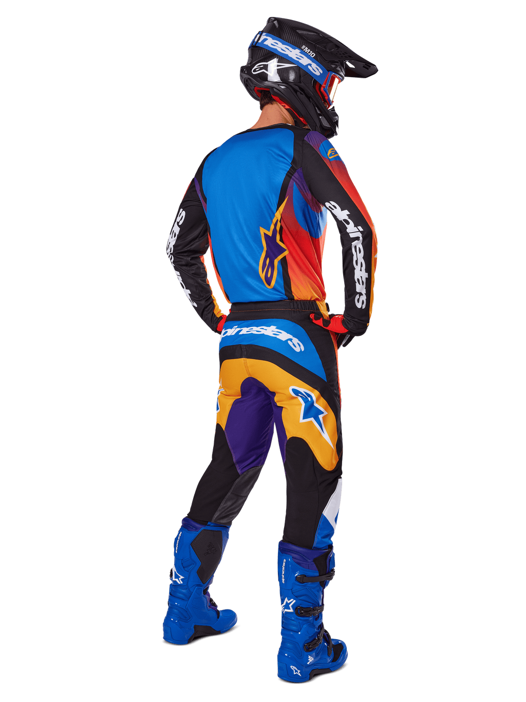 Motorcrosser van achteren gezien in de Alpinestars 2025 Fluid Wurx Gear Set, multicolor jersey met blauwe, oranje en paarse panelen, bijpassende broek met wit Alpinestars-logo op het zitvlak, felblauwe laarzen en een zwarte helm, geco'rdineerde outfit voor off-road racing