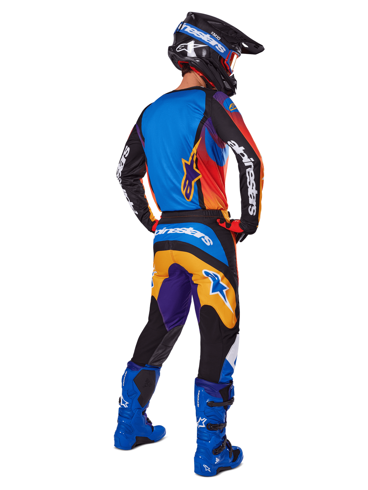 Motorcrosser van achteren gezien in de Alpinestars 2025 Fluid Wurx Gear Set, multicolor jersey met blauwe, oranje en paarse panelen, bijpassende broek met wit Alpinestars-logo op het zitvlak, felblauwe laarzen en een zwarte helm, geco'rdineerde outfit voor off-road racing