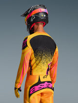 Alpinestars 2026 Techstar Nomur Jersey in Orange Yellow Pink, achteraanzicht van een motorcrosser in volledige uitrusting inclusief bijpassende broek en een zwarte helm, levendig ontwerp met gele en roze accenten en een zwart rugpaneel, atletische racepasvorm voor off-road prestaties