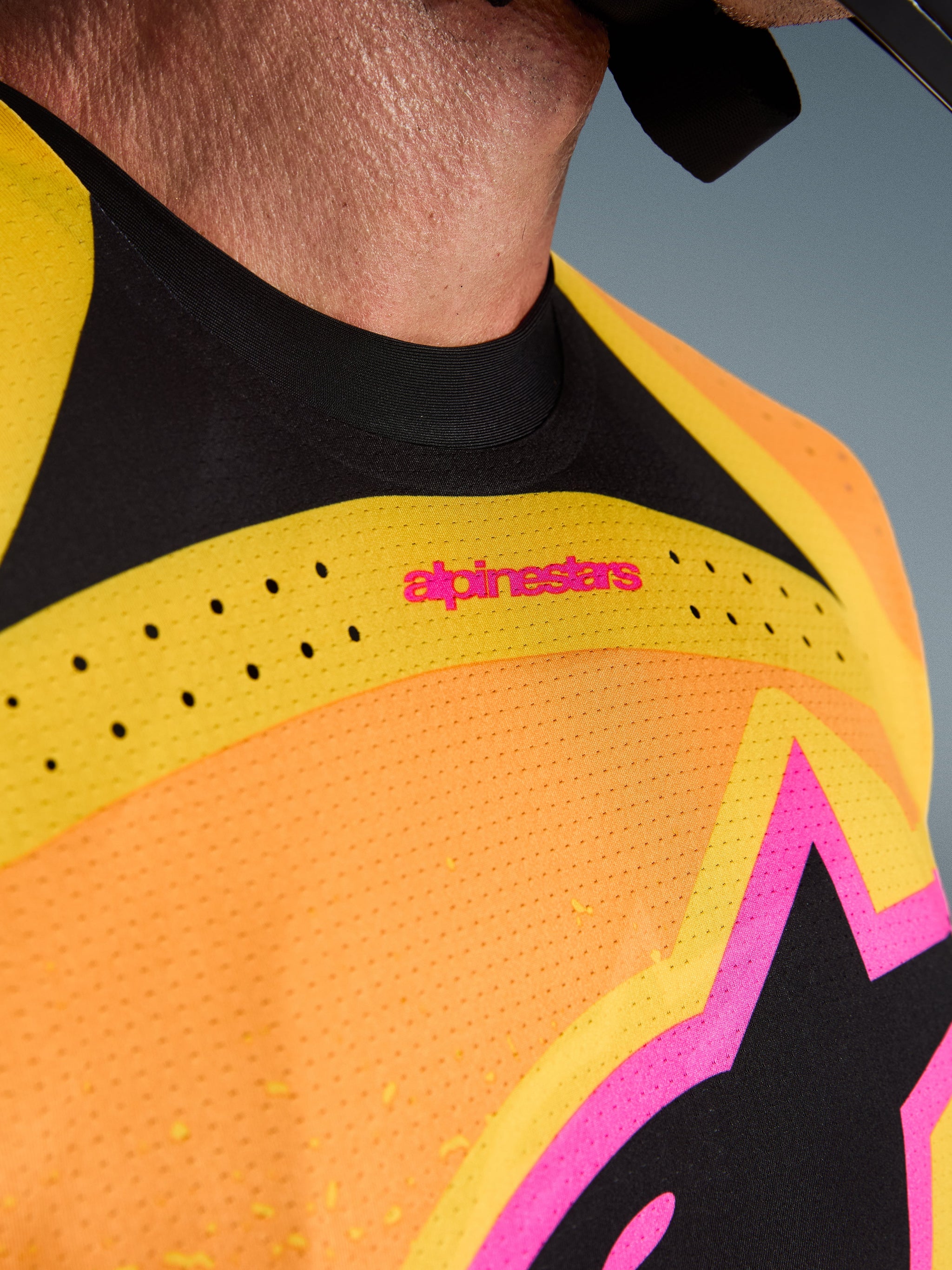 Alpinestars 2026 Techstar Nomur Jersey, motorcross shirt, oranje, geel en roze, close-up detail van de borst en de kraag, voorzien van lasergesneden ventilatie, roze branding en ademend mesh-materiaal