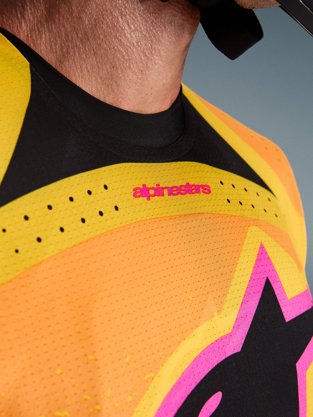 Close-up of the Alpinestars 2026 Techstar Nomur Jersey, Orange Yellow and Pink colorway, showing laser-cut ventilation perforations, seamless black collar, and pink branding details on perforated stretch fabric.