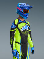 Motocrossrijder die de 2026 Techstar Nomur Jersey draagt in Dark Navy en Yellow Fluo, gecombineerd met een bijpassende broek, een blauwe racehelm en een crossbril, voorzien van een groot Alpinestars-logo en een sportieve racepasvorm voor off-road prestaties.