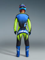 Rear view of a motocross rider wearing the Alpinestars 2026 Techstar Nomur Gear Set. The outfit includes a blue and neon yellow jersey with black spray-pattern accents, matching neon yellow and black pants featuring a large blue 'astars' logo on the seat, coordinated blue boots with white logos, and a blue and black helmet. Full professional racing gear designed for performance and visibility.