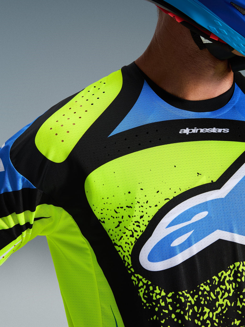 Alpinestars 2026 Techstar Nomur Jersey, motorcross shirt, fluogeel, donkerblauw en UCLA blauw, detailopname van de borst en schouder met lasergesneden perforaties voor ventilatie en het Alpinestars-logo, hoogwaardige off-road racekleding