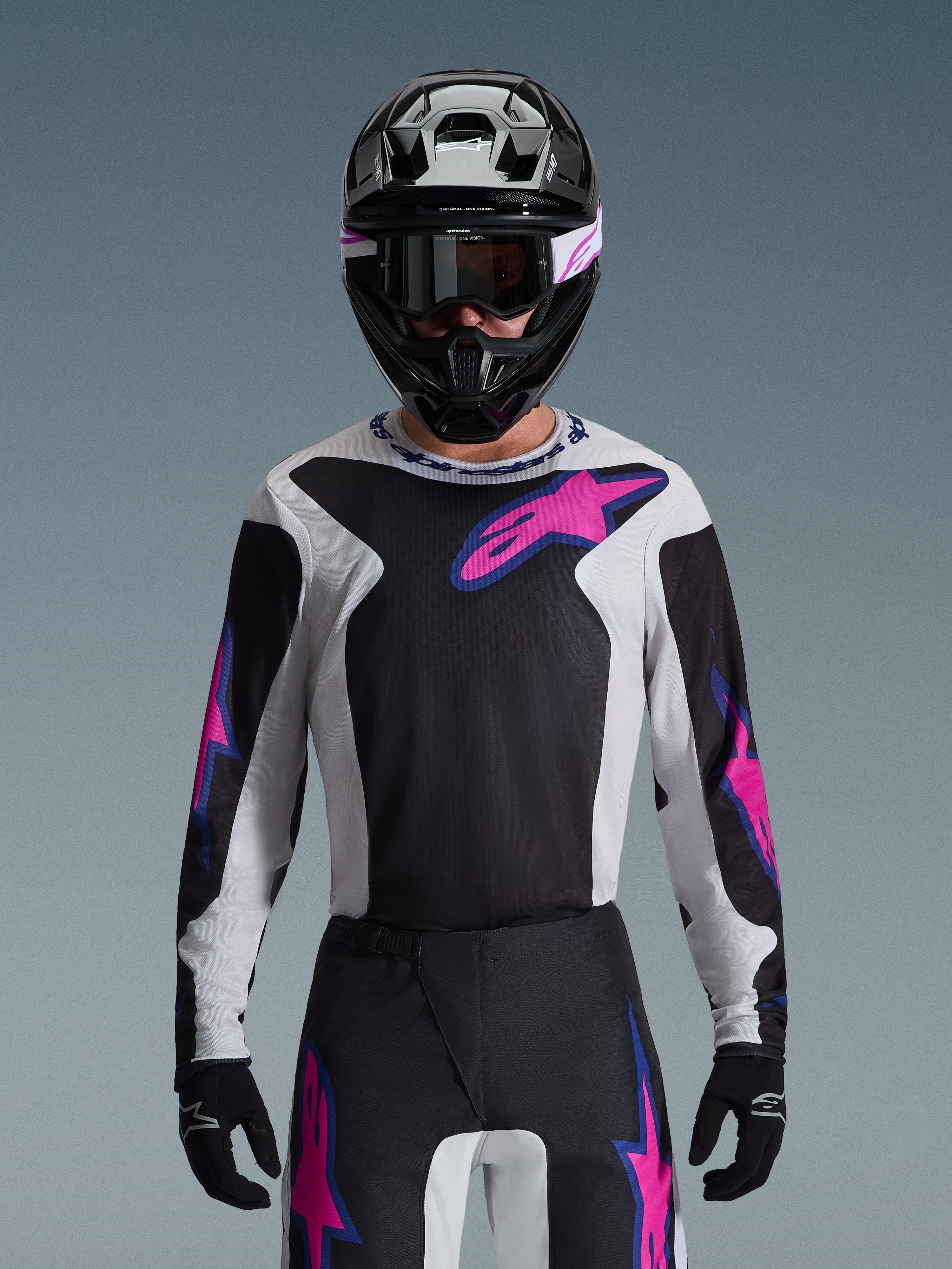 Alpinestars 2026 Fluid Grid Jersey, motorcross jersey, zwart, lichtgrijs en paars, gedragen door een rijder met bijpassende off-road broek, zwarte helm en crossbril, complete performance race-uitrusting