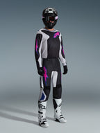 Motocross rider wearing complete racing gear, 2026 Fluid Grid Jersey in black with light gray and purple accents, matching Fluid Grid Pants, black helmet with coordinated goggles, white and black boots, and black gloves, professional studio setup for off-road racing.