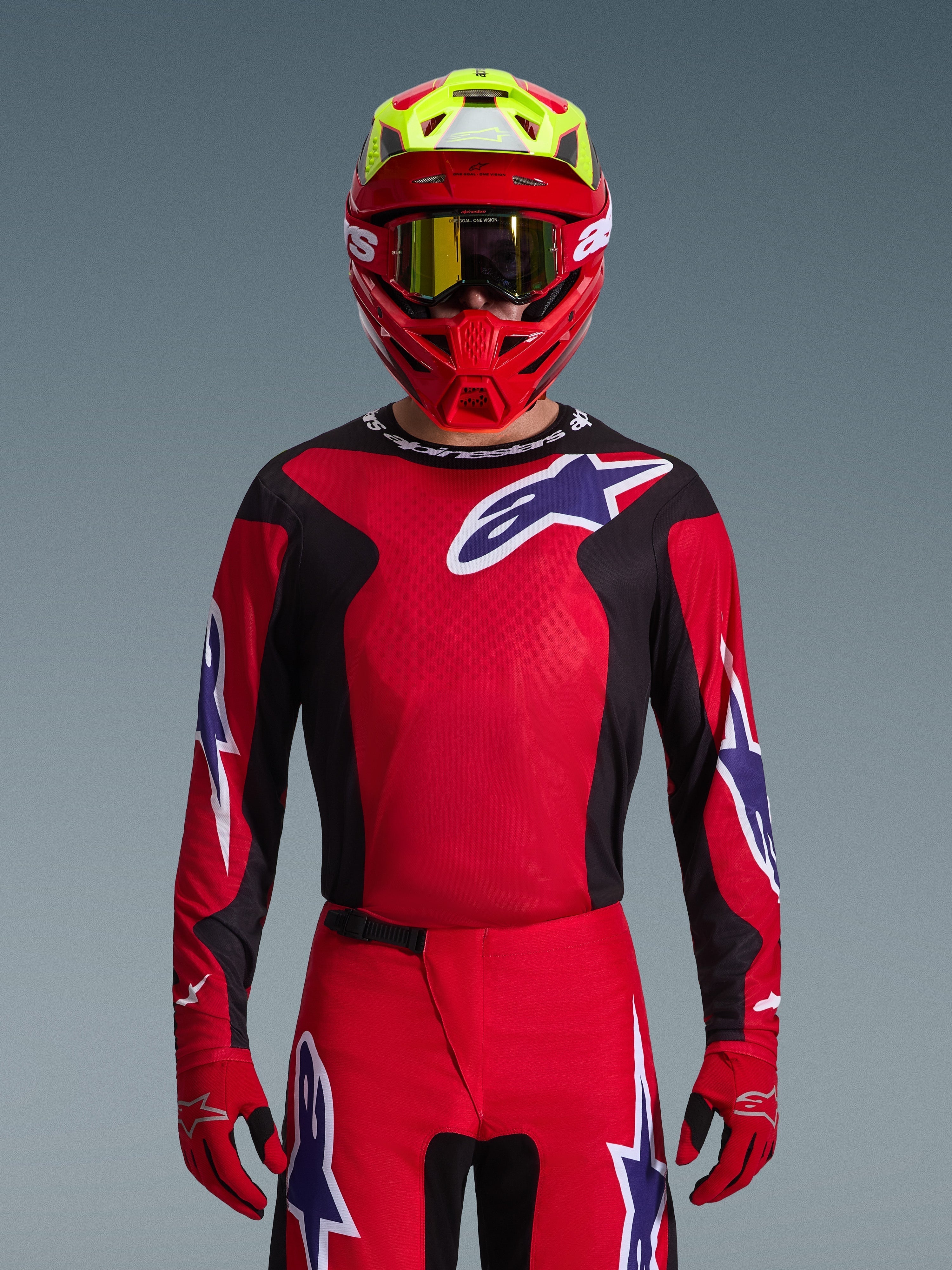 Alpinestars 2026 Fluid Grid Jersey, motorcross jersey, rood, zwart en paars, gedragen door een rijder met een rode en neongele helm en gouden crossbril, voorzien van grote sterlogo's op de borst en mouwen, gecoördineerde uitrusting voor off-road racen