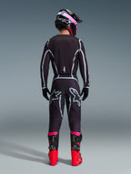 Motocross rider from the back wearing the Alpinestars 2026 Fluid Apex Jersey and matching pants in Black/Gray, featuring white geometric design lines and star logos on the seat, accessorized with a black and pink helmet and red and black racing boots.
