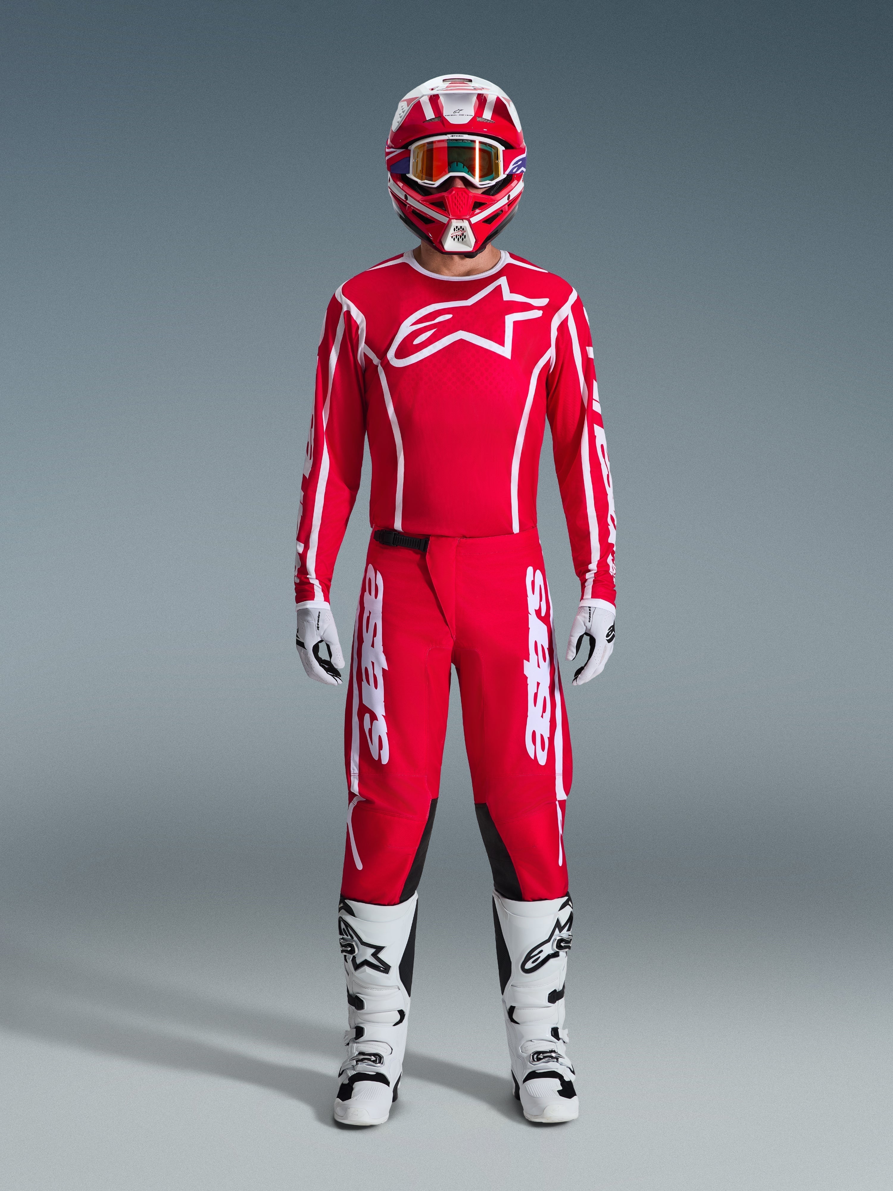 Motocross rider wearing complete 2026 Fluid Apex racing gear, Red jersey with white Alpinestars logo and sleeve branding, matching red pants with white accents and black panels, red and white helmet with mirrored goggles, white and black boots, and white and black gloves, professional gear set for off-road performance.