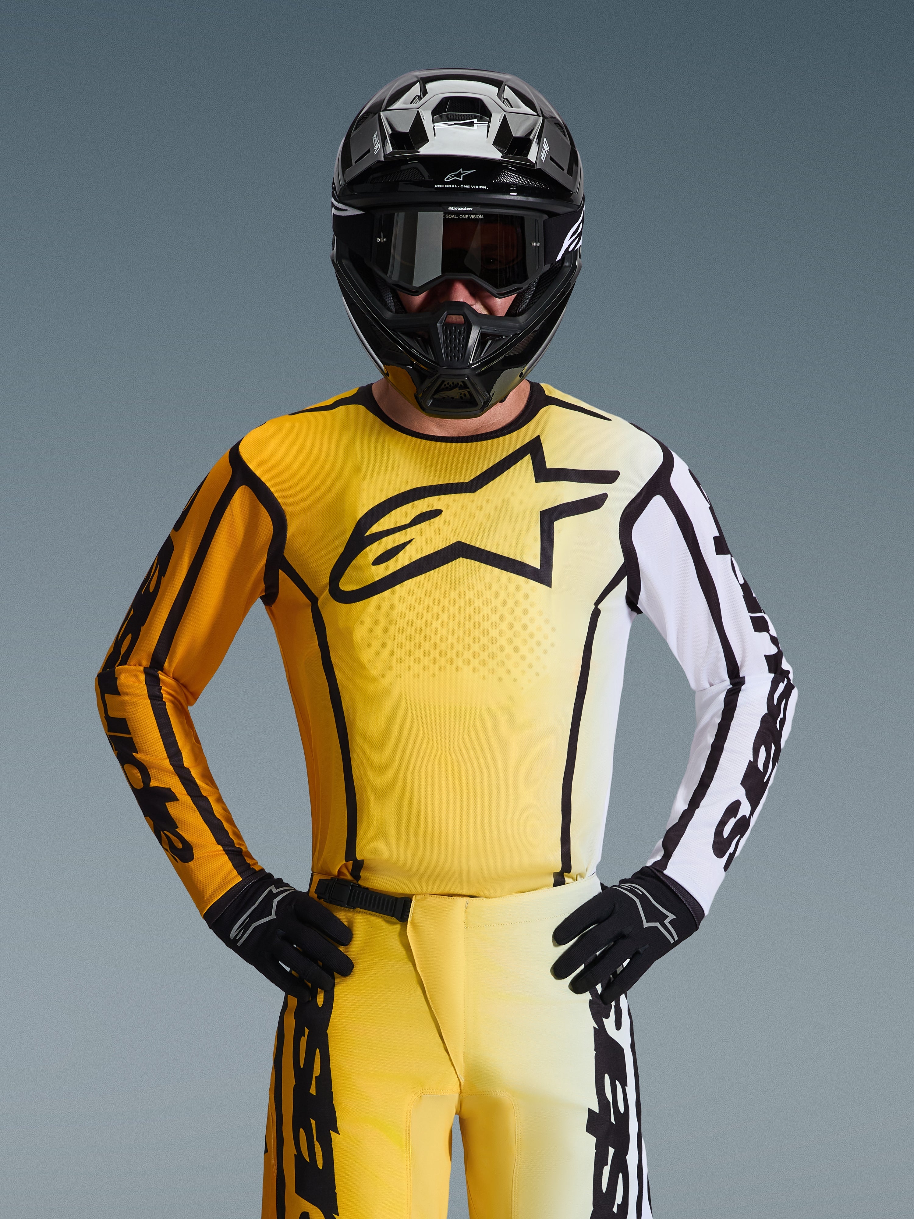 Alpinestars 2026 Fluid Apex Jersey, motorcross shirt, geel en zwart met een witte mouw en groot zwart logo op de borst, gedragen als onderdeel van een complete race-uitrusting met bijpassende broek, zwarte helm en handschoenen