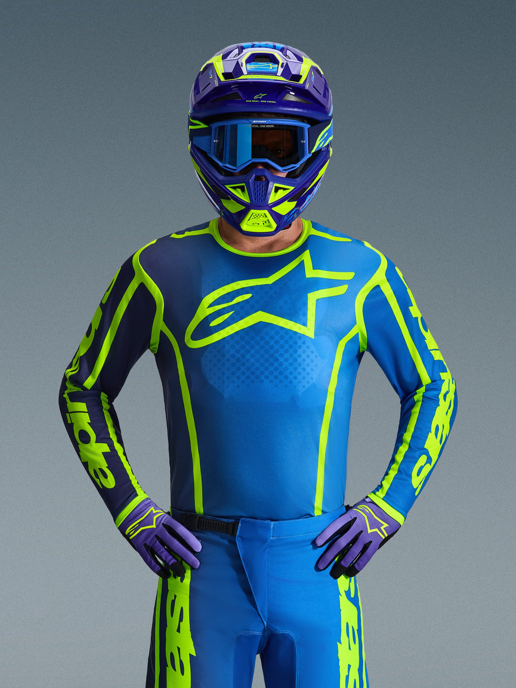 Alpinestars 2026 Fluid Apex Gear Set, Motocross rider wearing full protective gear, Teal blue jersey with neon yellow accents and a dark purple sleeve, matching teal pants and purple gloves, coordinated purple and neon yellow helmet with blue goggles, front view for off-road racing aesthetic