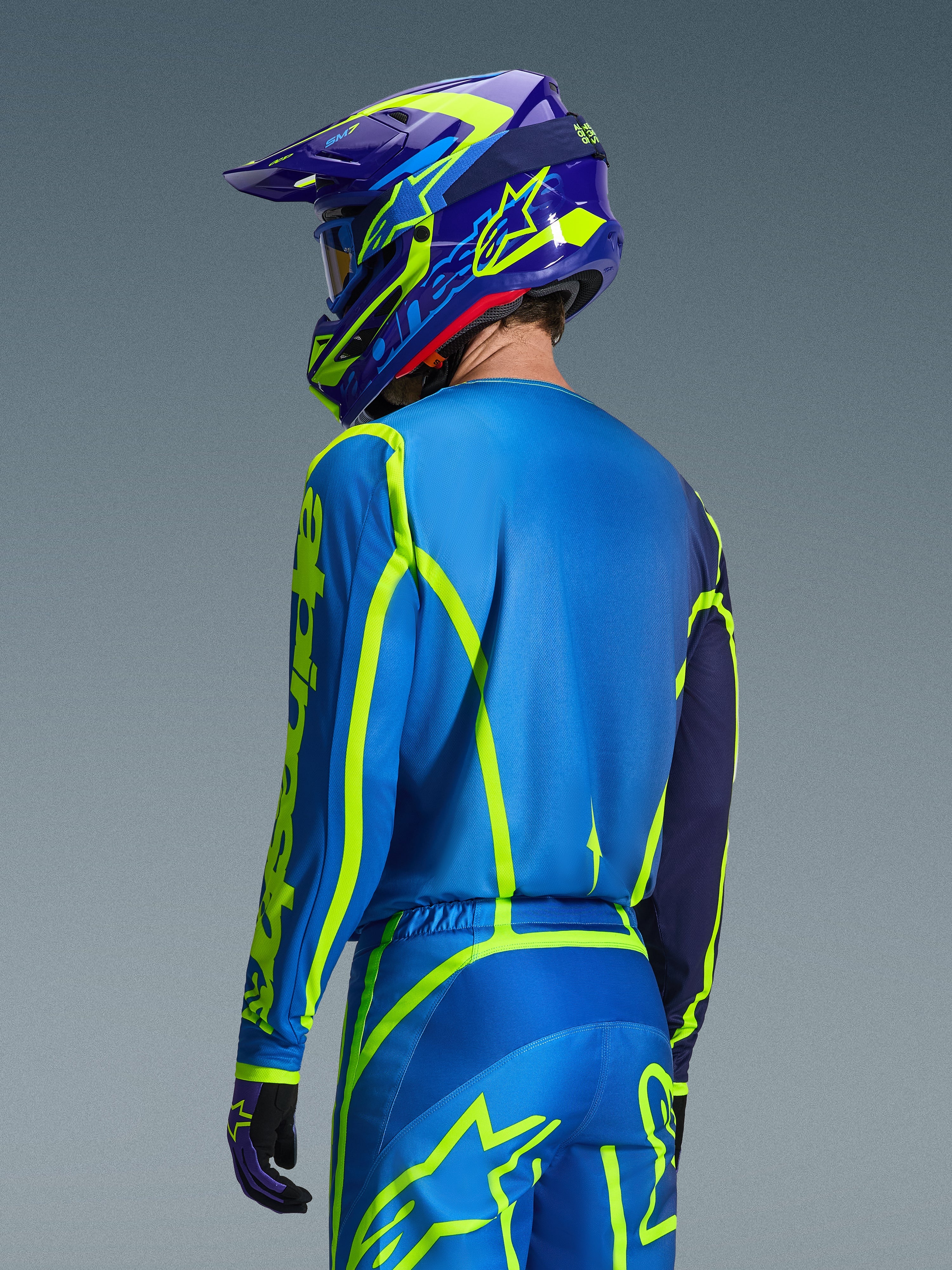 Alpinestars 2026 Fluid Apex Jersey, Blue Yellow Fluo, back view of rider wearing matching motocross pants and helmet, featuring fluorescent yellow geometric graphics and a relaxed athletic fit, coordinated off-road racing gear