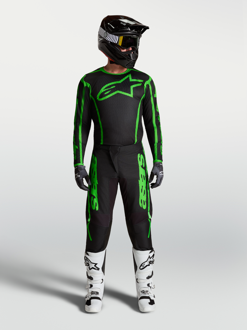 Alpinestars Fluid Apex V2 broek, heren motocrossuitrusting in zwart en fluogroen, volledige race-outfit met witte motorlaarzen en zwarte helm.