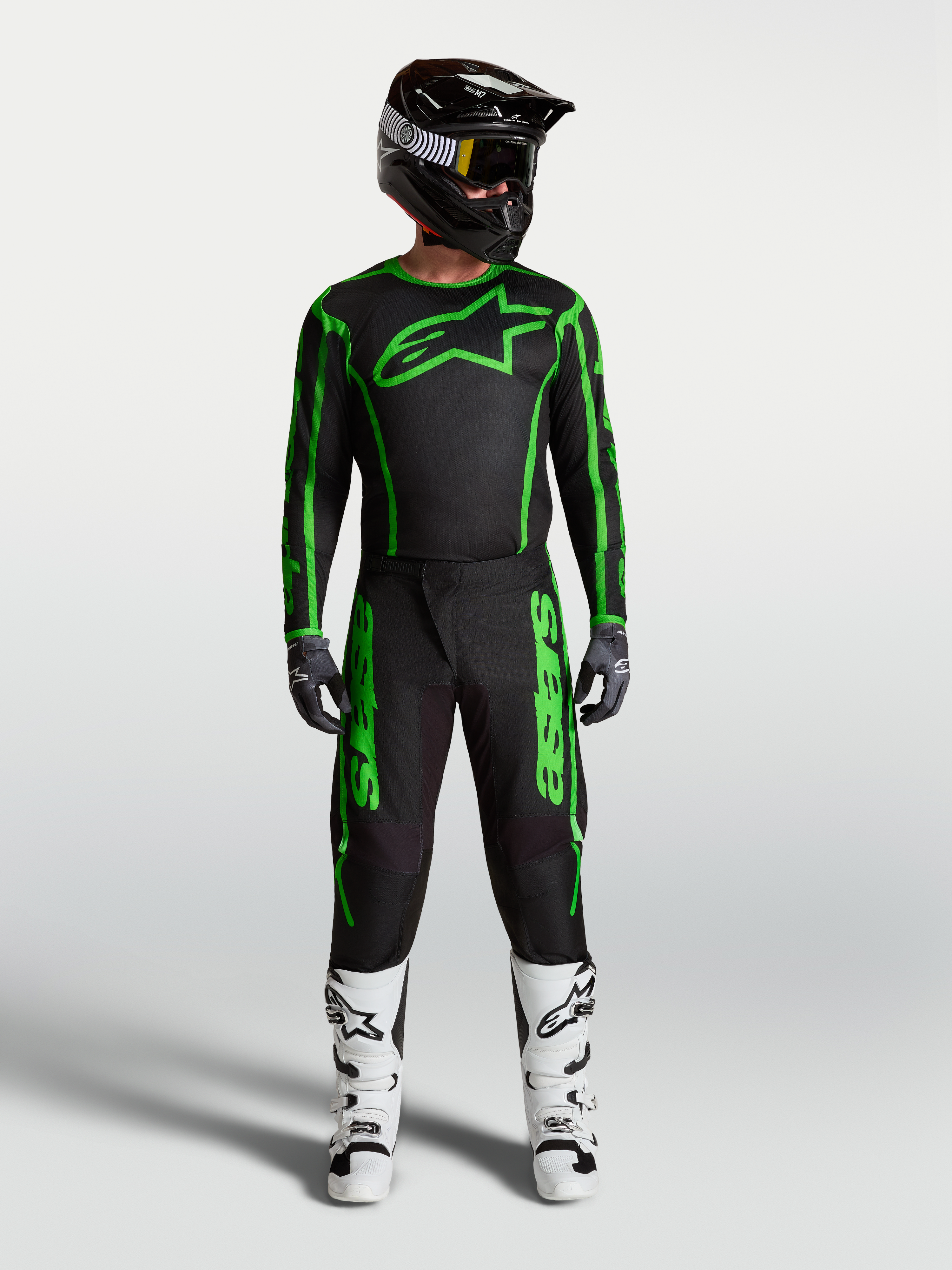 Alpinestars Fluid Apex V2 broek, heren motocrossuitrusting in zwart en fluogroen, volledige race-outfit met witte motorlaarzen en zwarte helm.