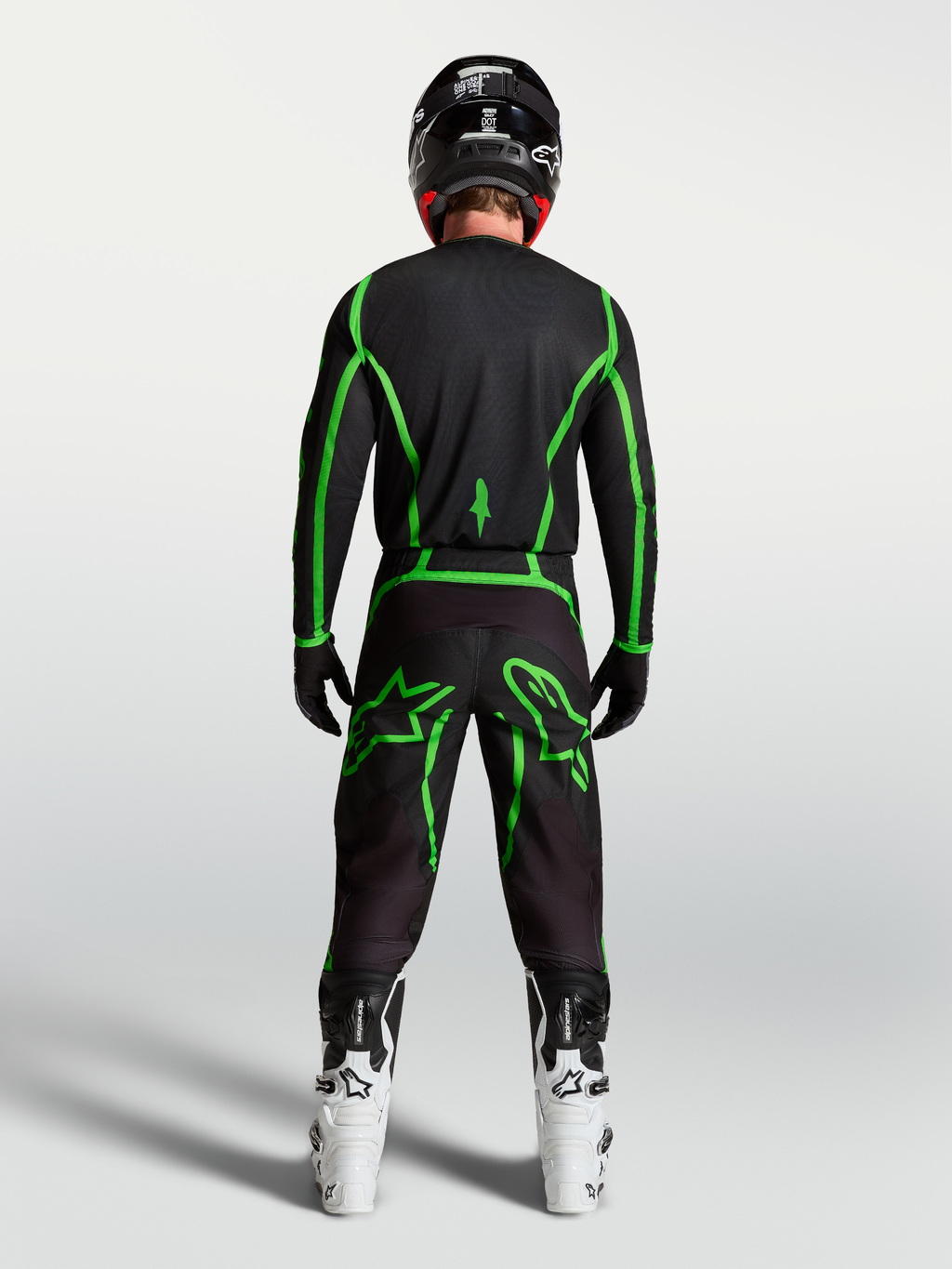 Alpinestars Fluid Apex V2 broek, zwarte en fluogroene motorcrossuitrusting van achteren gezien op een rijder met witte laarzen.
