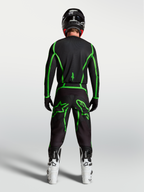 Alpinestars Fluid Apex V2 broek, zwarte en fluogroene motorcrossuitrusting van achteren gezien op een rijder met witte laarzen.