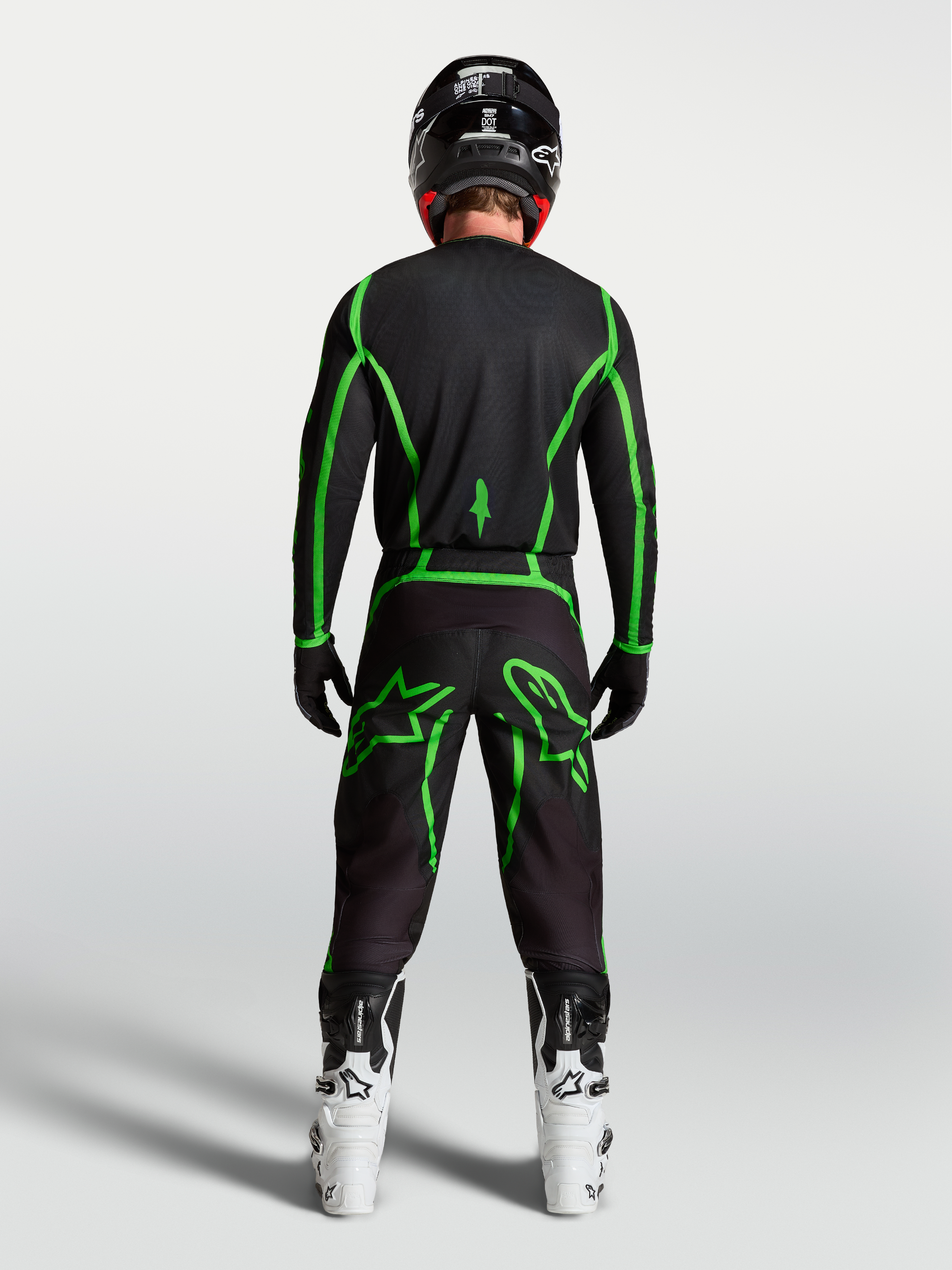 Alpinestars Fluid Apex V2 broek, zwarte en fluogroene motorcrossuitrusting van achteren gezien op een rijder met witte laarzen.