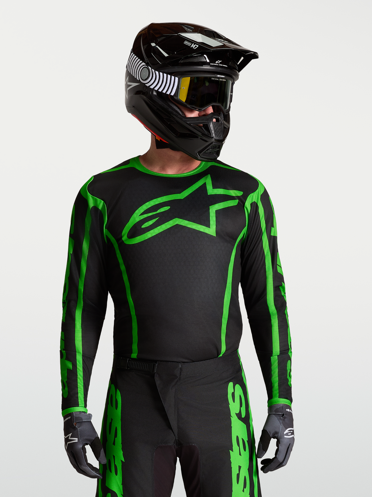 Alpinestars Fluid Apex V2 Jersey, zwart en groen fluo motocross-top, gedragen op model met helm, vochtafvoerende polyfabric, atletische pasvorm.