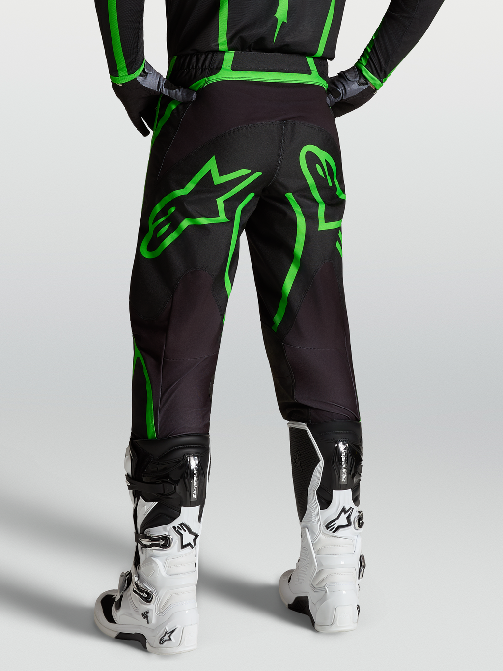 Alpinestars Fluid Apex V2 Broek, heren MX en off-road motorkleding, zwart en fluogroen, achterzicht op model met witte laarzen.