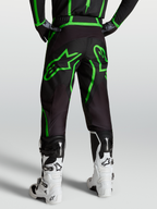 Alpinestars Fluid Apex V2 Broek, heren MX en off-road motorkleding, zwart en fluogroen, achterzicht op model met witte laarzen.