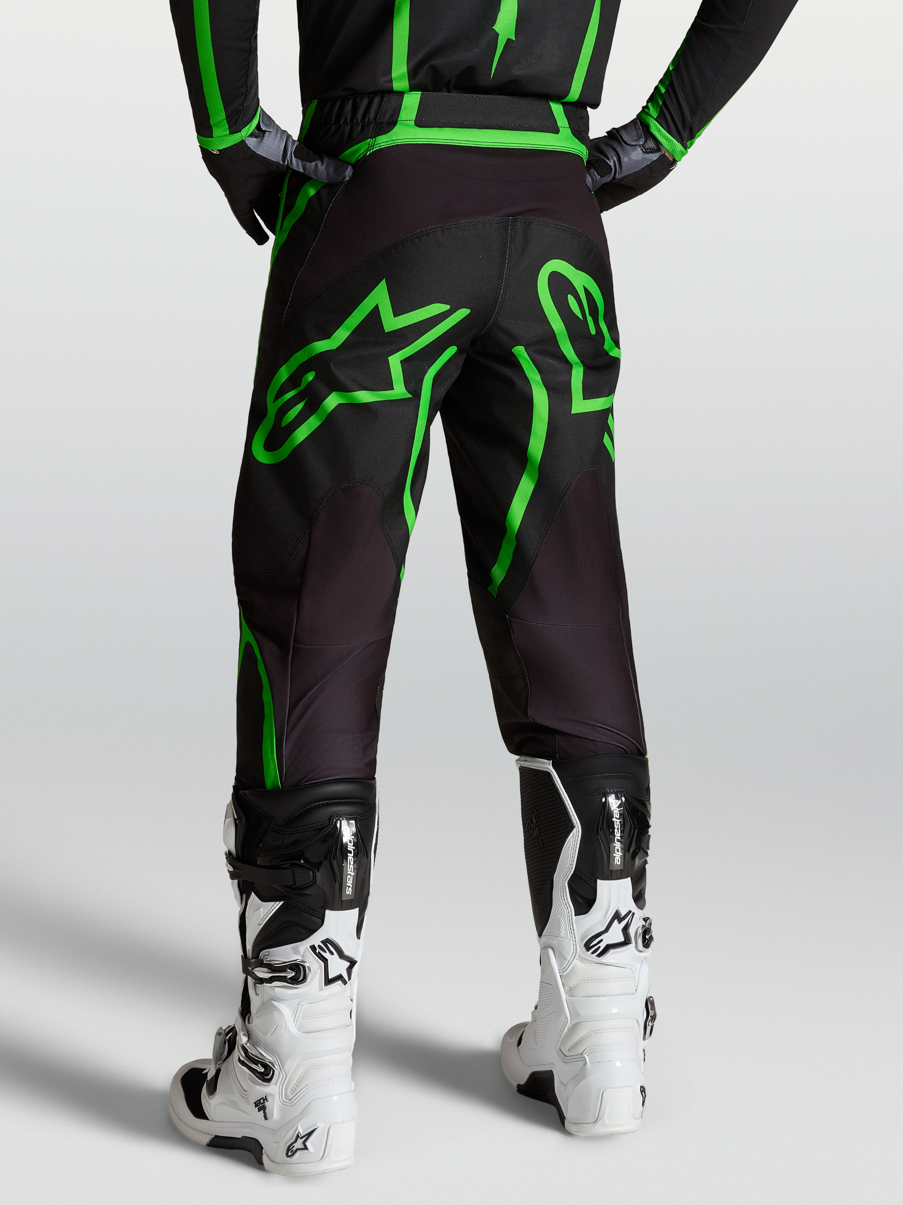 Alpinestars Fluid Apex V2 Broek, heren MX en off-road motorkleding, zwart en fluogroen, achterzicht op model met witte laarzen.